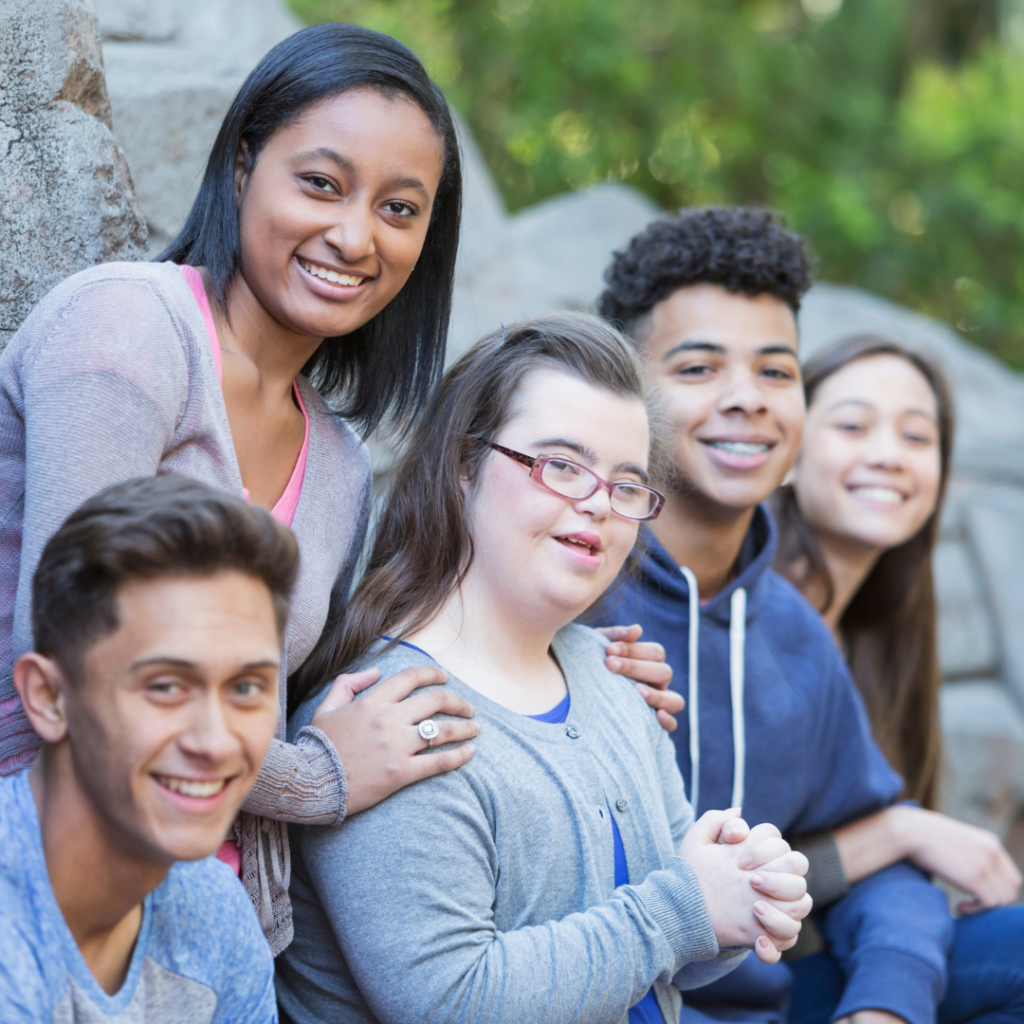 Group of young adults, one with Down syndrome, smiling at the camera. 