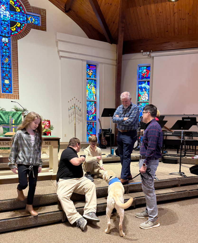 boy with yellow lab mix service dog in a church with people around him